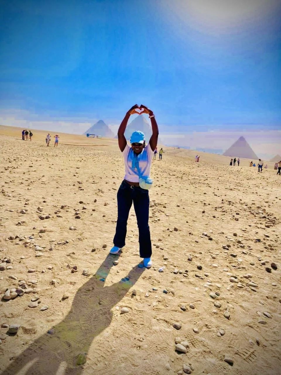 The founder making a heart with her hands in the desert, with the pyramids of Giza behind her
